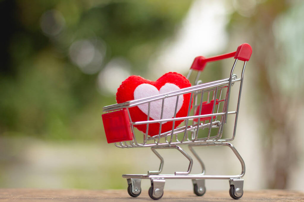 Forma di cuore rosso nel carrello della spesa in miniatura sul tavolo in legno concetto di amore per San Valentino. - Foto, immagini