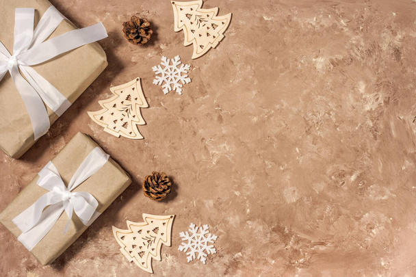 Keret felső nézet gúnyolódni karácsonyi ajándék doboz fehér szalaggal, fenyőtoboz és fából készült herringbone dekoráció. Lapos feküdt bézs texturált háttér másolási hely. - Fotó, kép