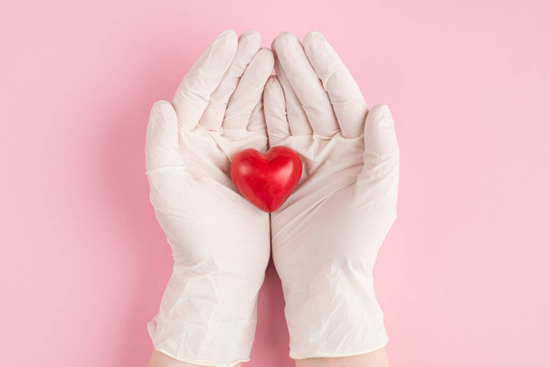Boven boven overhead pov eerste persoon close-up bekijk foto van rood hart in de handen van vrouwelijke arts in handschoenen geïsoleerd op pastel roze achtergrond met copyspace - Foto, afbeelding
