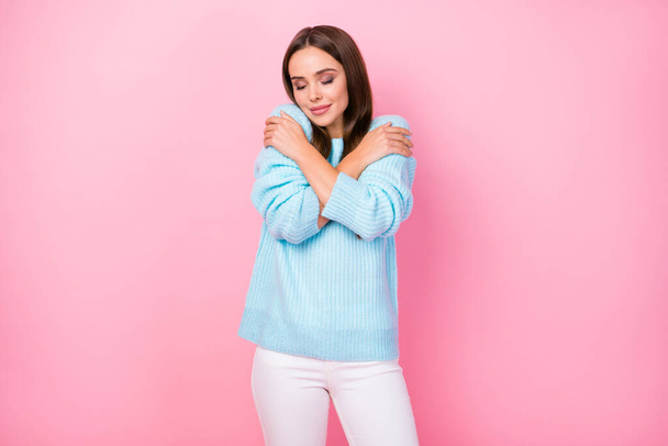 Photo of attractive charming lady hold herself hugging shoulders amazing soft cloth pullover eyes closed wear knitted blue sweater white pants isolated pastel pink color background - Zdjęcie, obraz