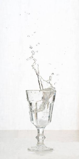 Vintage-Glas mit prickelndem Wasser mit Spritzern. Konzept von Flüssigkeitsspritzern und Aktion im Stillleben - Foto, Bild