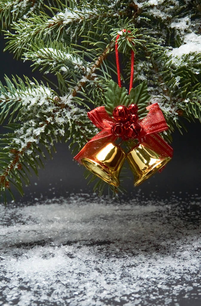 Χριστουγεννιάτικη διακόσμηση με καμπάνες, κλαδί χριστουγεννιάτικου δέντρου και τεχνητό χιόνι σε μαύρο φόντο - Φωτογραφία, εικόνα