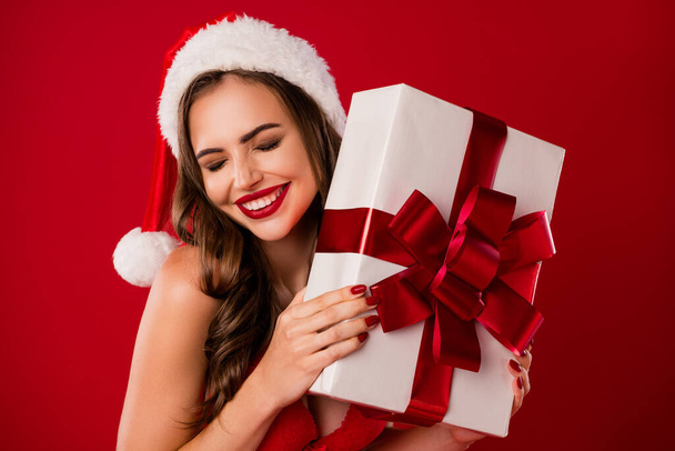 Portrait of adorable santa helper arms hold present closed eyes winter headwear isolated on red color background - Photo, Image