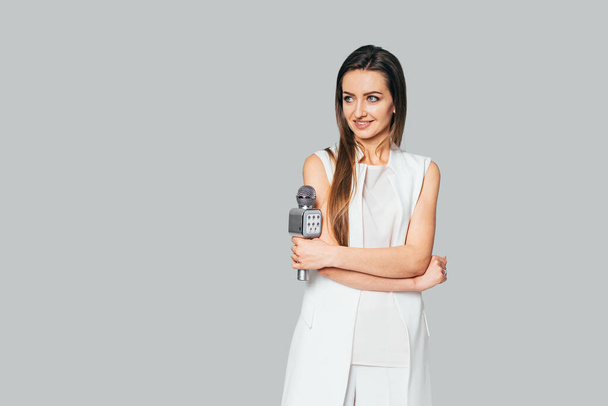 Presentation, public speech, conference, broadcasting, advertising. Cheerful young woman, reporter, TV presenter holding microphone. Isolated on gray background. - Φωτογραφία, εικόνα