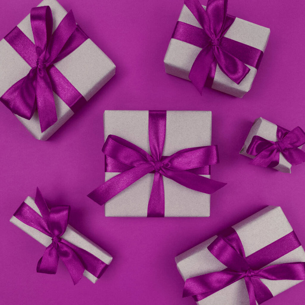 Gift boxes wrapped in a craft paper with purple ribbons and bows. Festive monochrome flat lay. - Photo, image
