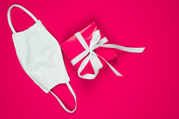 Christmas greeting card with gift box and protective mask on pink background. Female blog concept. High quality photo - Fotoğraf, Görsel