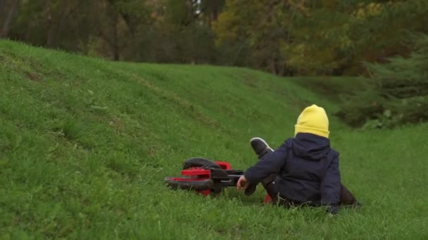 Back view video of a caucasian boy falling down while riding a bike in a green field and getting up to continue - Footage, Video