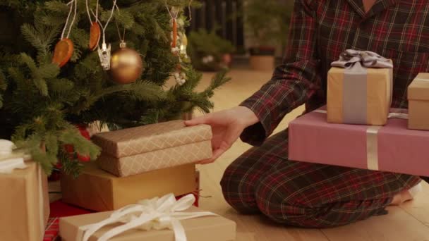 Πλάνα από το κέντρο με γυναικεία χέρια να βάζουν τυλιγμένα χριστουγεννιάτικα δώρα κάτω από διακοσμημένο χριστουγεννιάτικο δέντρο παραμονή Πρωτοχρονιάς - Πλάνα, βίντεο