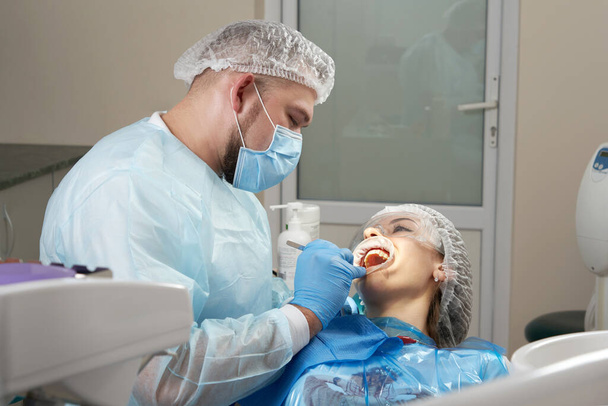Dentista haciendo un tratamiento dental en una paciente femenina. Dentista examinando los dientes de un paciente en la oficina de odontología moderna - Foto, imagen