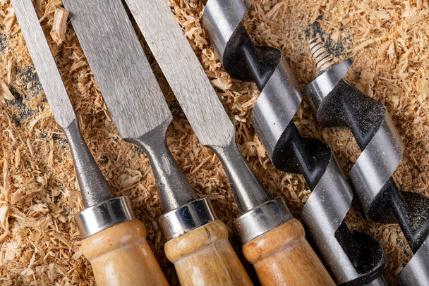 Chisels and wood drills laid on sawdust. Carpentry accessories in the workshop. Dark background. - 写真・画像
