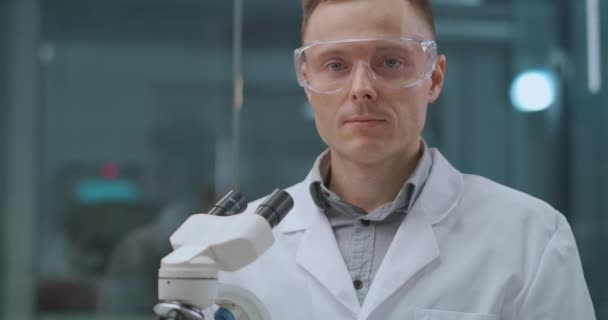 portré magabiztos laboratóriumi technikus férfi dolgozó szobában, védőszemüveget visel, közel áll a mikroszkóp - Felvétel, videó