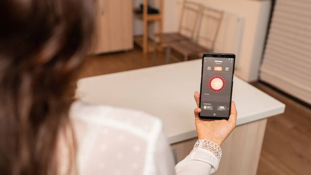 Donna in cucina casa utilizzando app telefono per controllare a distanza il sistema di illuminazione - Foto, immagini