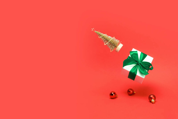 冬のバナー。金色の冬の木、緑色の弓を持つ白いギフトボックスは、暗赤色の背景にクリスマスの組成物に赤いボールと輝くライトで落ちます。装飾、テキストのコピースペース. - 写真・画像