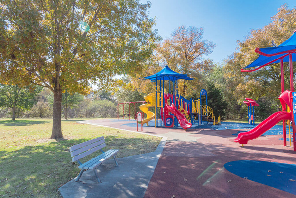 Colorido parque infantil público cerca del parque natural con colorido follaje de otoño en Flower Mound, Texas, Estados Unidos. Equipo de recreación para niños con vela de sombra y tema de bomberos rojos - Foto, Imagen