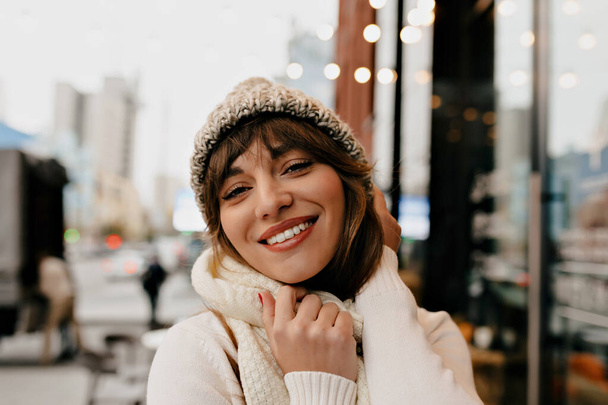 Fille heureuse en tenue d'hiver élégante posant dans un café extérieur avec extérieur moderne. Photo de femme caucasienne joyeuse appréciant vacances. Photo de haute qualité - Photo, image