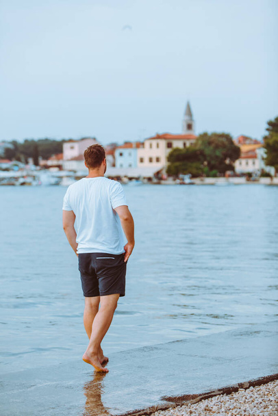 man walking by sea beach in summer evening fazana town on background in croatia. vacation concept - Фото, изображение
