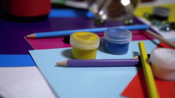 Pöydällä on satunnaisesti järjestetty Avocarel maalit, lyijykynät, harjat, värillinen paperi - Materiaali, video