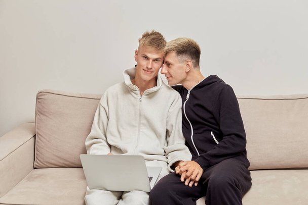 Cute gay couple sitting at home on the couch in their pajamas. LGBT couple. - Foto, imagen