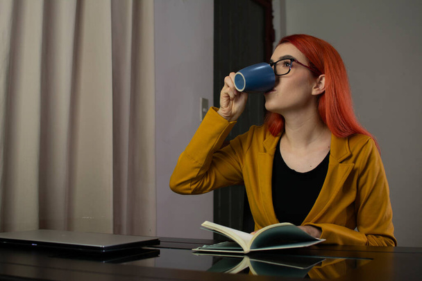 Mujer leyendo un libro y tomando una taza de café después de trabajar en casa - Foto, imagen