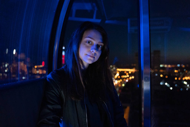 Young happy woman sitting in ferris wheel booth riding on attraction, blue light - Foto, afbeelding