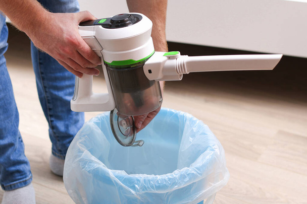 A man uses a bagless vertical cordless vacuum cleaner to clean the floor. - Foto, Bild