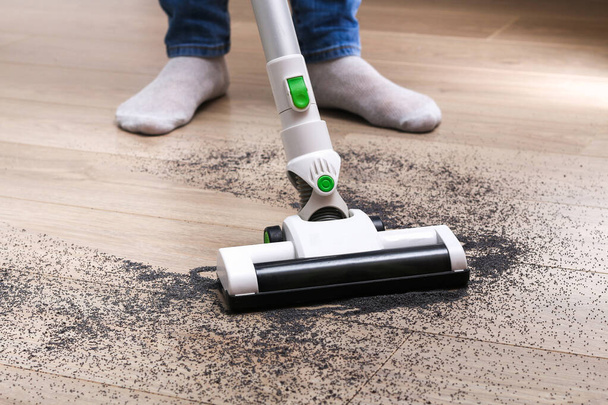 A man uses a bagless vertical cordless vacuum cleaner to clean the floor. - Foto, afbeelding