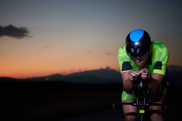 triathlon athlete cycling fast riding professional racing bike at night - Valokuva, kuva