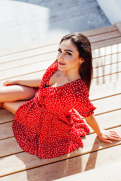 Hermosa mujer morena de moda en vestido rojo de verano se sienta en los pasos - Foto, Imagen