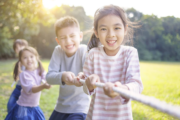 Szczęśliwe dzieci bawią się w przeciąganie liny w parku - Zdjęcie, obraz