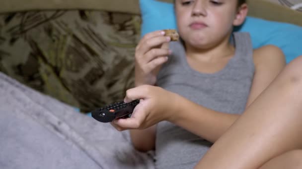 Bambino affamato premere i pulsanti con le dita sul telecomando TV, mangiare torta a letto - Filmati, video
