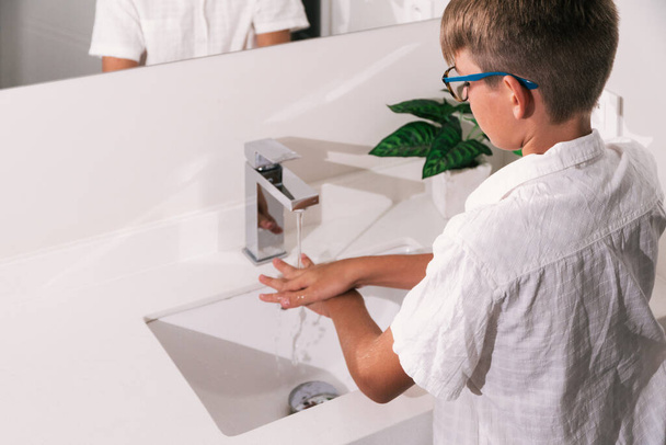 Стокове фото симпатичного хлопчика, який використовує мило і воду, щоб очистити руки у ванній
. - Фото, зображення