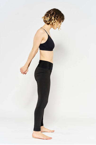 mujer deportiva en jeans negros y una camiseta haciendo ejercicios en una habitación luminosa - Foto, Imagen
