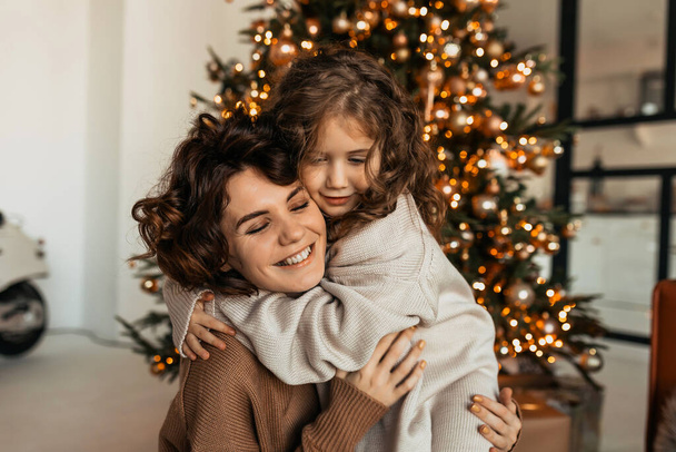 Чарівна приємна біла жінка з кривими обіймається зі своєю маленькою донькою і святкує Різдво і Новий рік. Високоякісна фотографія
 - Фото, зображення