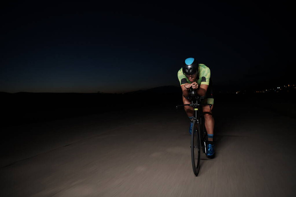 triathlon athlete cycling fast riding professional racing bike at night - Fotoğraf, Görsel