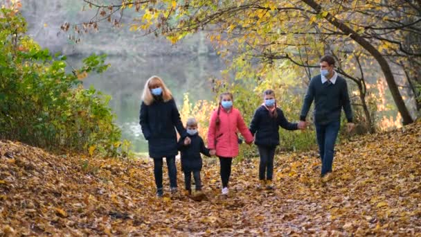 Család, orvosi maszkos szülők sétálnak a parkban egy őszi napon. séta a kovid-19 koronavírus pandémia idején. - Felvétel, videó