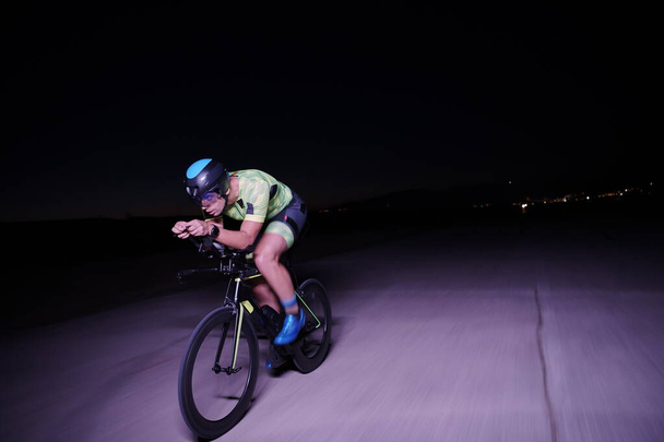 triathlon athlete riding bike fast at night - Foto, Bild
