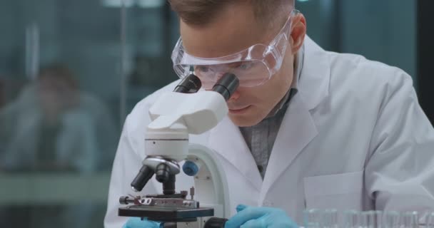 hombre experto forense está investigando análisis y evidencias en el laboratorio, mirando al microscopio, explorando la sangre - Metraje, vídeo