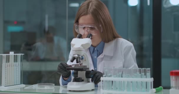 лаборант просматривает анализ коронавируса в лаборатории, рассматривает в медицинском микроскопе - Кадры, видео