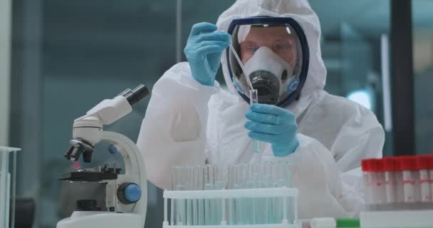 férfi tudós dolgozik veszélyes és mérgező vegyi anyagok kémiai laboratóriumban, védő ruha, maszk és kesztyű - Felvétel, videó