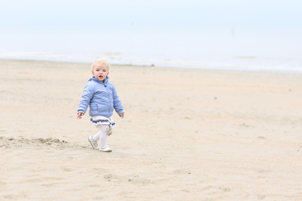 Baby girl walks on peaceful sandy autumn beach - Photo, image
