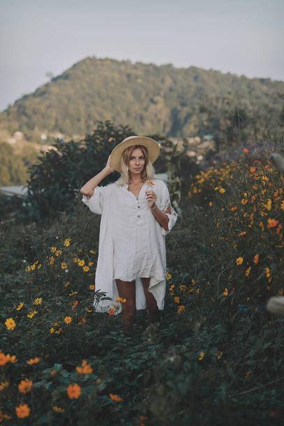 The blonde in a linen dress walks among herbs and wildflowers on a meadow in the mountains - Fotografie, Obrázek