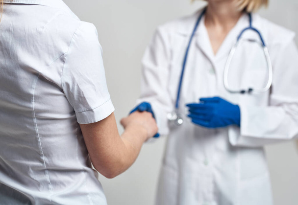 Медсестра пожимает руку пациенту на светлом фоне и голубые перчатки со стетоскопом - Фото, изображение
