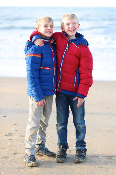 Brothers in warm colorful coats standing on the beach - Photo, image