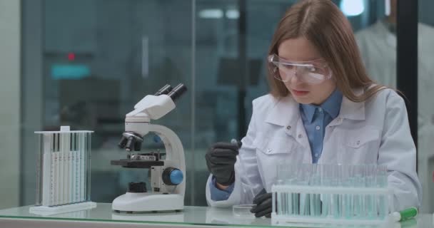 Химическая лаборатория, женщина-техник тестирует вещество, применяя в пластине для исследования под микроскопом - Кадры, видео