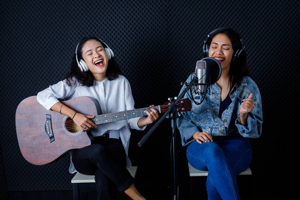 Happy cheerful pretty smiling of portrait of Two young Asian woman vocalist Wearing Headphones with a guitar recording a song front of microphone in a professional studio - Photo, image