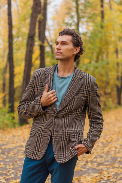 Tall handsome man dressed in a brown jacket walking on the autumn alley - Fotografie, Obrázek