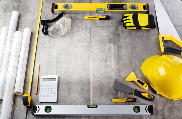 Contractor concept. Tool kit of the contractor: yellow hardhat, libella, hand saw. Plans and notebook on the gray tiles background. - Photo, Image
