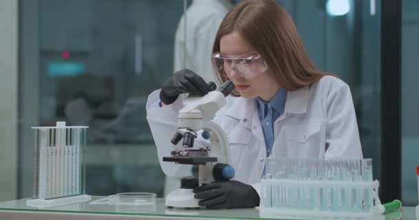 junge Gesundheitsexpertin arbeitet im Labor und testet neuen Impfstoff von covid-19 mit modernem Mikroskop - Filmmaterial, Video
