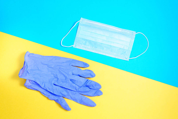 コロナウイルスに対する予防保護。手袋青い黄色の背景の医療面マスク。流行時の健康概念。上からの眺めは平らで - 写真・画像