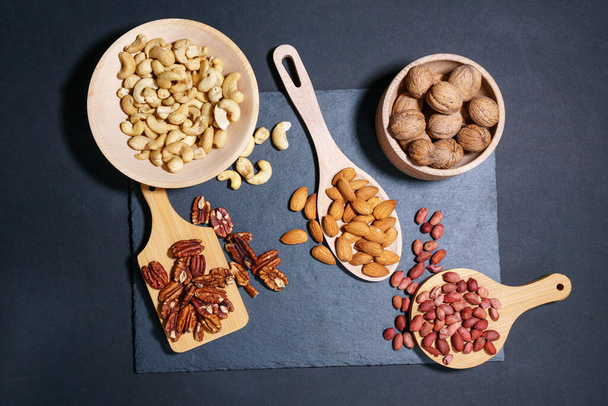 Pekannüsse, Mandeln, Cashewnüsse, Erdnüsse, Walnüsse, Pinienkerne auf schwarzem Hintergrund flach gelegt - Foto, Bild